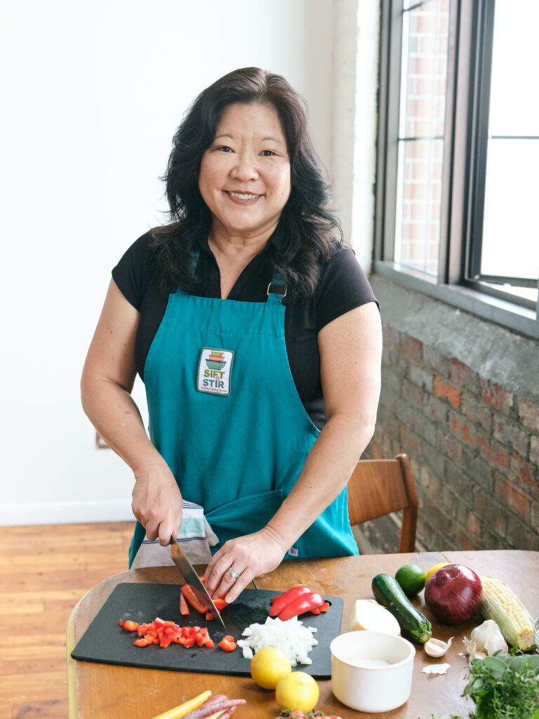 Asian woman wearing an apron and chopping vegetables